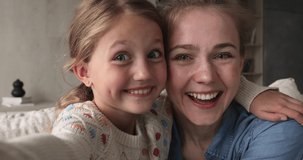 Funny faces of young mother and cute preteen girl daughter cuddling looking at front web camera of smartphone shooting video blog. Two sisters elder and younger hug pose for hilarious selfie together
