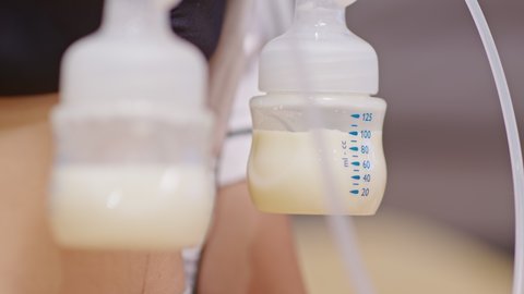 Mother using breast milk pump for baby. Close up Milk from breast pump dropping into milk bottle storage for baby newborn.