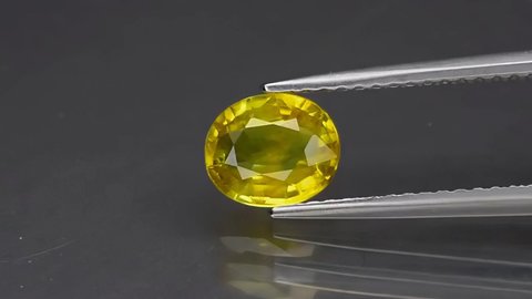 natural yellow sapphire gemstone in the tweezers