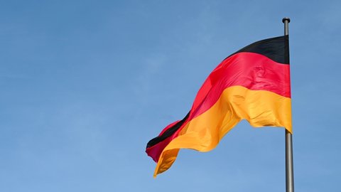 Slow motion of German flag flying on the wind. Waving flag on flagpole against blue sky in Germany. Black, red and yellow colors on German flag in a front of Bundestag. Symbol of German people. 