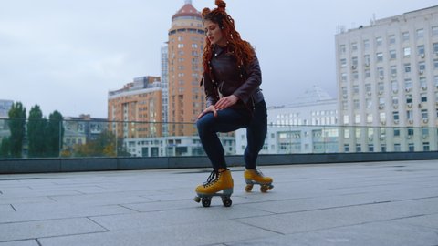 Stylish sporty woman dancing on roller skates at rooftop. Smiling roller skater spinning on urban background. Active hipster girl enjoying roller skating lesson outside. Street sports concept.