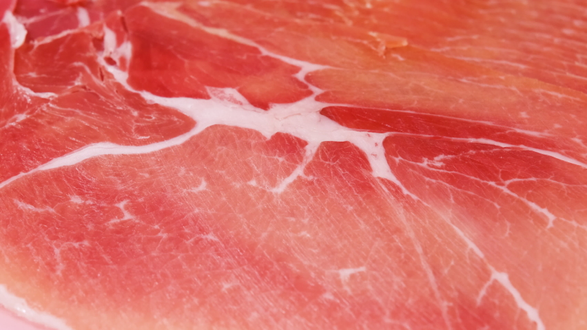 Jamon or dry-cured ham produced in Spain texture close up. 4K resolution Food background. Hand in glove take thin slice of jamon