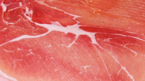 Jamon or dry-cured ham produced in Spain texture close up. 4K resolution Food background. Hand in glove take thin slice of jamon