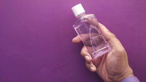  hand hold a mouthwash liquid container against purple background 