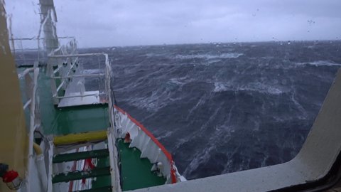 Ship in storm. A lot of splashes. View from bridge. Ship climb up wave. Strong pitching. High waves hit ship. White foam on water. Very strong storm. Bow breaks waves