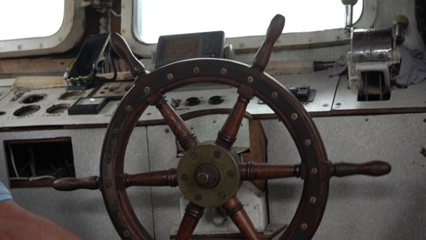 Wooden steering wheel is turned by hand. Steering wheel turns left and right. Old tug inside. Bridge of an old boat