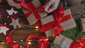 female woman hands wrapping Christmas presents gift box with brown craft paper, tying red ribbon bow on wooden desk with new year ornaments: stars light garland and green coniferous. top view DIY home - Powered by Shutterstock - Get 15% off with code: PIKWIZARD15