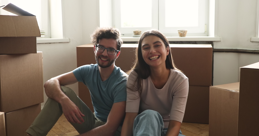 Portrait proud family couple start new life at own rented flat tenancy leasehold property look at camera show key. Young spouses bloggers real estate buyers sit on floor broadcast live at social media Royalty-Free Stock Footage #1083055348