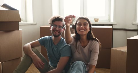 Portrait proud family couple start new life at own rented flat tenancy leasehold property look at camera show key. Young spouses bloggers real estate buyers sit on floor broadcast live at social media