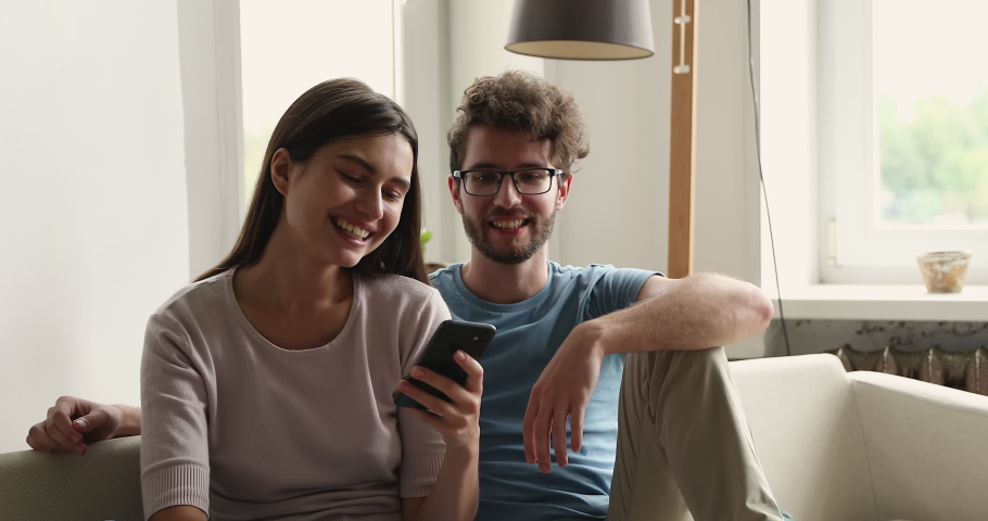 Choosing variants. Friendly young married couple buyers engaged in discussing online shop offers using cell. Happy millennial husband wife talk swipe virtual electronic catalogue pages on smartphone