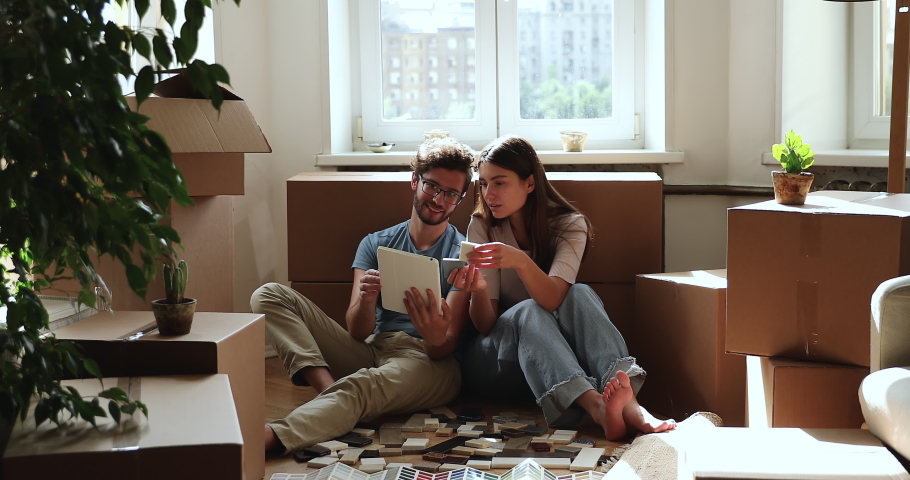 Inspired married couple do renovation at own apartment sit on floor among packed belongings choose materials online use tile samples paper web catalogues on pad. Excited homeowners redecorate new flat Royalty-Free Stock Footage #1083055399