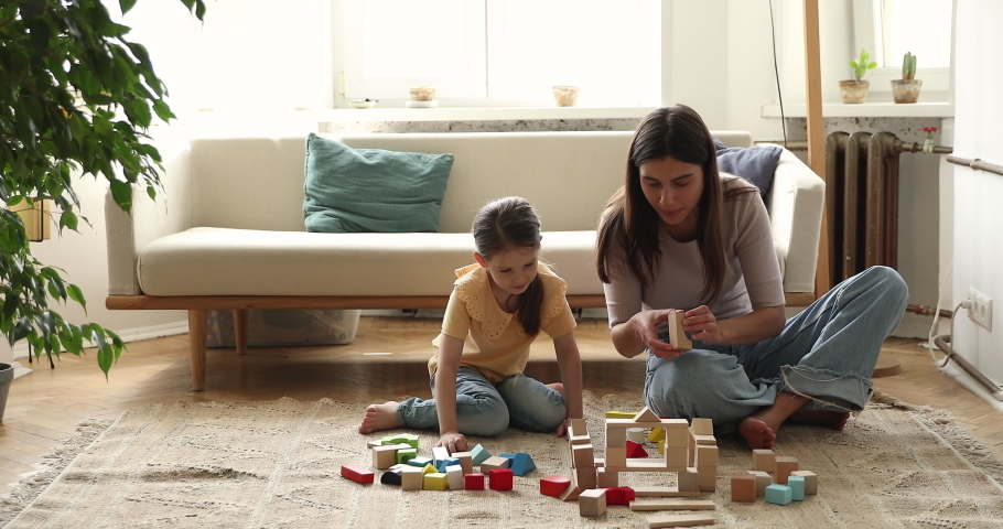 Young mom nanny older sister spend time with little girl preschooler have fun play wooden constructor set on warm floor at living room. Mother daughter child enjoy making house from bricks at playtime Royalty-Free Stock Footage #1083058162