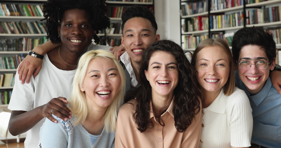 Group of young 17s happy multi ethnic college students smiling look at camera, posing in modern university library. Portrait of laughing friends different race and culture. Friendship, gen Z concept | Shutterstock HD Video #1083066172