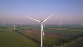 Windmills with rotating wings among green fields. Wind farm with turbine cables for wind energy. Renewable energy source, earth care. Drone video of wind power station, 4k. Botiyevska Ves, Ukraine.