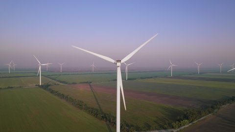 Windmills with rotating wings among green fields. Wind farm with turbine cables for wind energy. Renewable energy source, earth care. Drone video of wind power station, 4k. Botiyevska Ves, Ukraine.