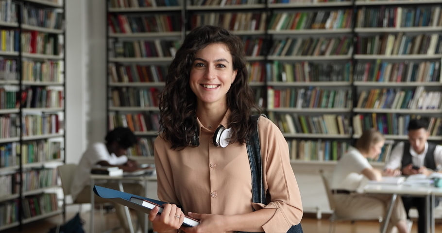 Portrait of attractive young teenager student girl holding folder and notepad posing standing in campus library. College or university education, professional skill, knowledge, studentship concept Royalty-Free Stock Footage #1083071680