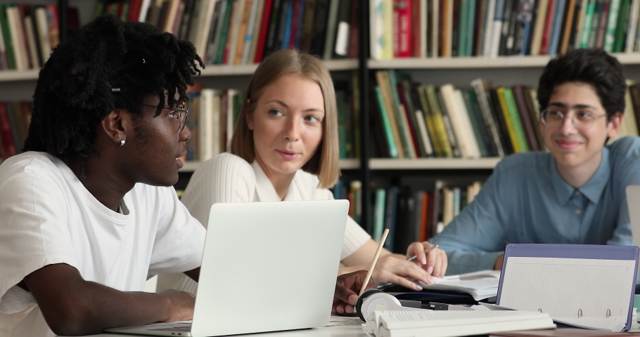 Diverse attractive friendly students sit at desk in library writing essay, discuss collaborative project, preparing for high school exams and chatting. Friendship, university education, study concept Royalty-Free Stock Footage #1083071734