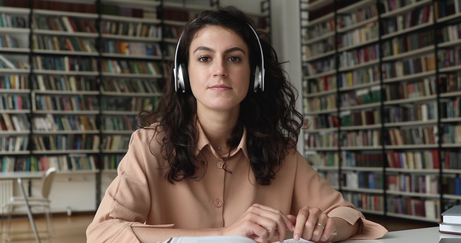Student girl sit in library wear headphones talks to tutor, take part in online class, distancing studies, learn foreign language gain new knowledge use modern tech. Video call event, tuition concept Royalty-Free Stock Footage #1083071767