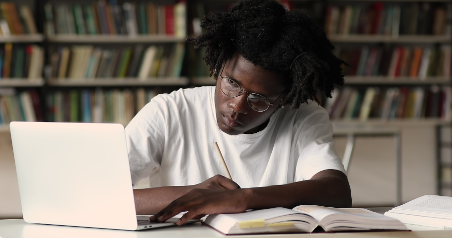 African student in glasses sit in library take notes studying with laptop, make assignment, use internet resource website, e-learn busy in self-education. Prepare for exams, gen Z, modern tech concept Royalty-Free Stock Footage #1083071776
