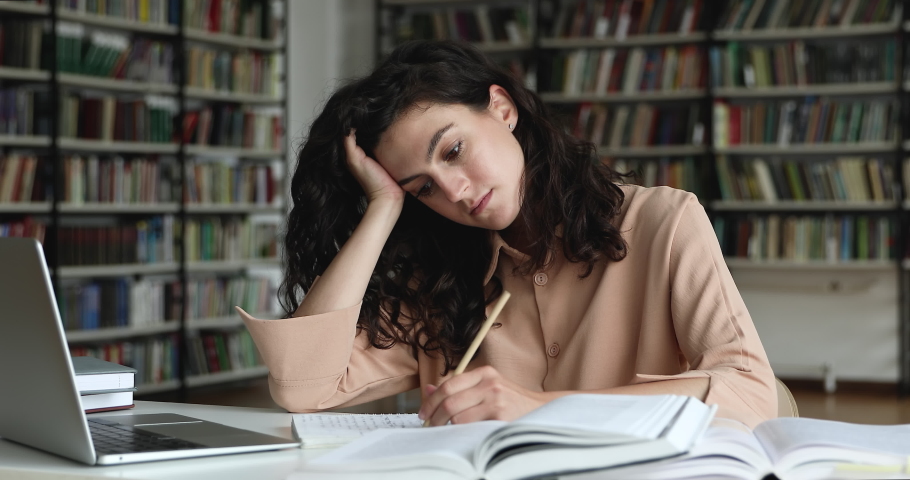 Young tired unmotivated girl student sit at table in library prepares for exam test, feeling lack of ideas while makes coursework. Boring study, monotonous learning, unloving subject at school concept Royalty-Free Stock Footage #1083072115