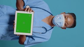 Nurse holding tablet with horizontal green screen, wearing face mask against coronavirus. Medical specialist using modern device with chroma key, mockup template and isolated background.