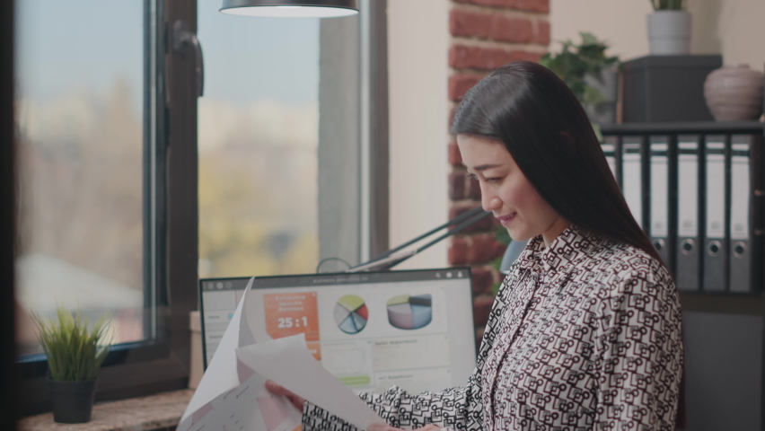 Company employee looking at papers and computer to work on project planning. Woman designing business startegy with documents and charts. Handheld shot of entrepreneur doing analysis