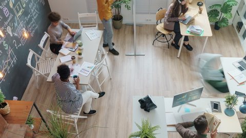 Zoom-in high angle view of diverse creative team working in shared office talking cooperating using laptops writing on chalkboard wall Video stock