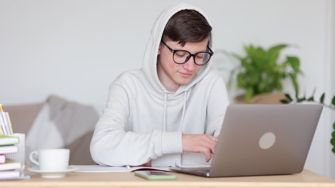 Remote education of teen scholars. Smiling teen boy with spectacles waves spbi hand to greet classmates at online lesson via laptop at workplace in living room 4k video
