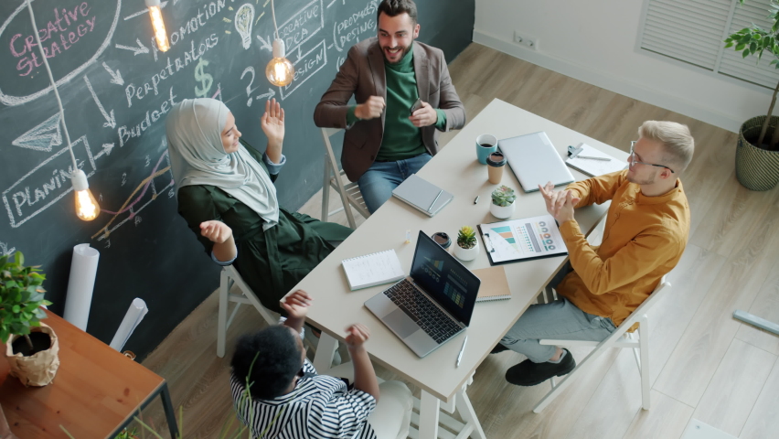 Joyful employees are getting good news on mobile phone laughing doing high-five in office sharing positive emotions. Work and success concept.