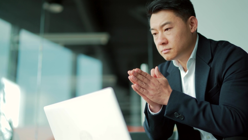 Portrait thoughtful Asian businessman working on a laptop computer at a modern office desk. Confident Focused pensive man in formal suit indoors. thinking of inspiration solving a problem. Startup Royalty-Free Stock Footage #1083084748