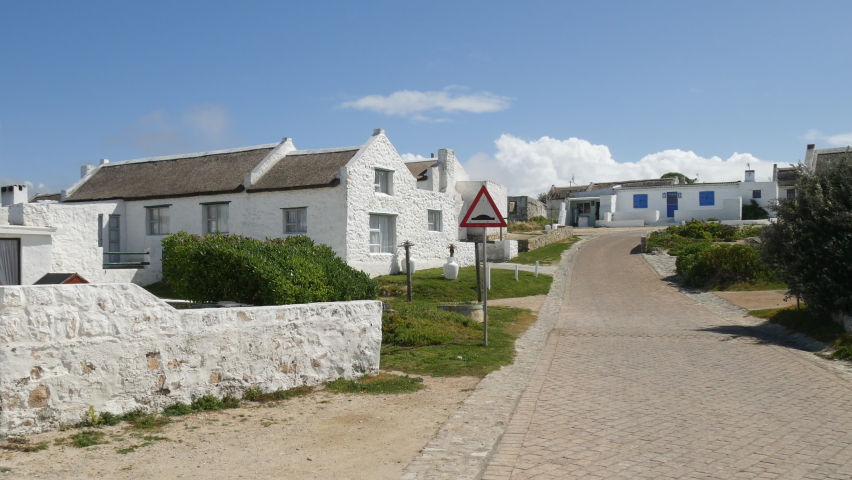 Lime washed thatch cottages main entrance street at Anniston fishing community national monument, pan, with blue sky white clouds, dog appears left bottom frame 