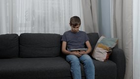 Teenage boy using digital tablet computer sitting on couch at home. Kid using application for learning, playing games, browsing internet, looking video, studying online