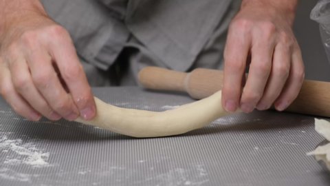 4K Close-up of the chef's hands cut a strip of dough into pieces and roll them in flour. Preparation of dough for modeling flour products with filling.
