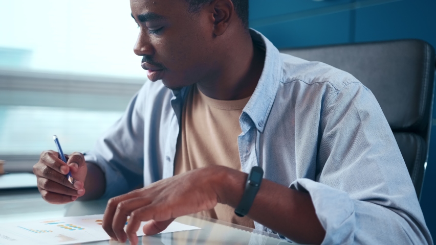 Serious young African American businessman checking corporate paperwork correspondence sitting at office desk. Male entrepreneur reading documents, analyzing financial papers, preparing audit report. Royalty-Free Stock Footage #1083088927