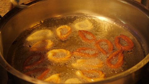 Close-up of donuts fried in boiling oil in the restaurant kitchen, the cook takes out ready-made donuts from the oil with special tongs.