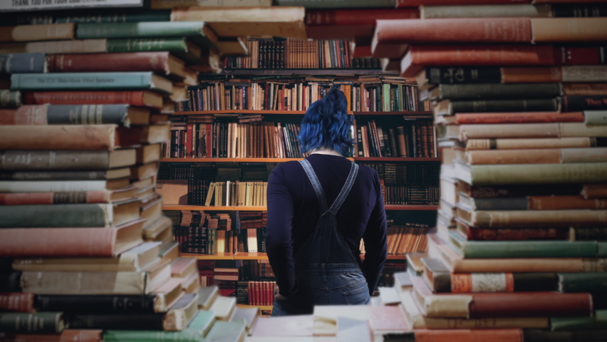 Girl Inside Library Choosing Books Zoom In Through Stack of Books. Camera Zooming through a stack of books with a woman inside the library with many book shelves. Royalty-Free Stock Footage #1083094243
