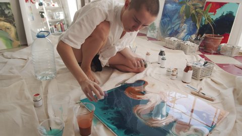 Professional artist spending time in her studio creating new artwork in fluid art technique adding paints and spreading them