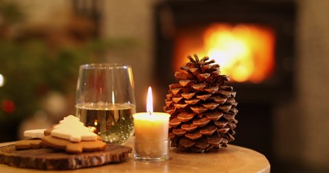 Cozy evening with glass of wine, candles, fire, pine cone and fire with Christmas tree in the background.