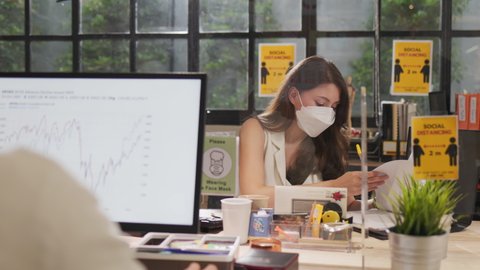 Young people with face masks back at work in office after lockdown.Asian small business startup  meeting with laptop and chart paper everyone mask for covid19 protection corona.