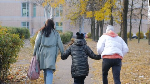 A woman with two daughters hurries to school, a view from the back of the girls running with their mother along the autumn alley.