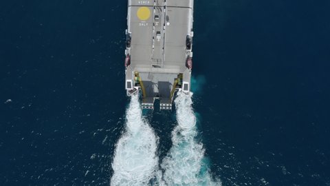 Modern high speed fast ferry aerial view from above. Ferry ship reach destination entering a port. Top down drone view of cargo passenger ship turning in blue water. Vessel engines leaving white foam