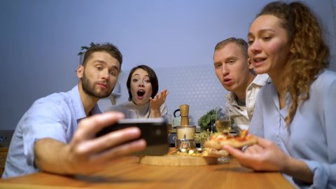 happy friends eating pizza together, four young students enjoying a festive lunch meeting time sitting at the table and video chatting on smartphones New normal lifestyle, social distancing concept
