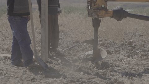 Tractor drill the ground. Drilling rig drills the ground, two workers help shovels. Machine drilling holes in the ground. Close up of auger. drilling a hole into the ground. Slow Motion 