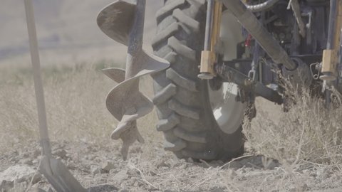 Tractor drill the ground. Drilling rig drills the ground, two workers help shovels. Machine drilling holes in the ground. Close up of auger. drilling a hole into the ground. Slow Motion 