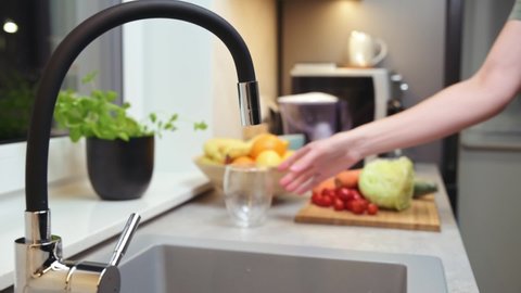 Woman pouring water from faucet into glass at the kitchen
