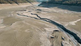 Drone view of earth textures caused by global warming and climate change. Small amount of water slowly moving across the paths. Mountains stretching in the distance. 4K Video