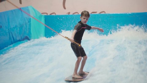 Child and instructor at Flow Rider indoor surfing training session. Teenager on water board training on simulator wave indoors. Young surfer during training on generated waves. Water sports
