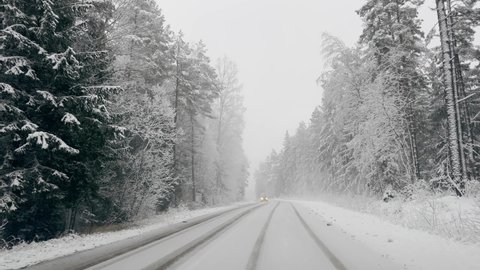 POV person driving past another car during heavy snowfall along country road with winter trees around