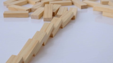 Domino effect, row of wooden domino falling down on white background. Dominoes falling in a row, hand pushes a Domino and starts a chain reaction Board game.