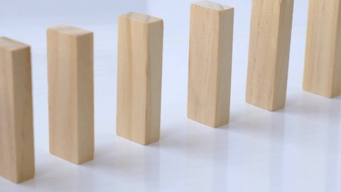 Domino effect, row of wooden domino falling down on white background. Dominoes falling in a row, hand pushes a Domino and starts a chain reaction Board game.